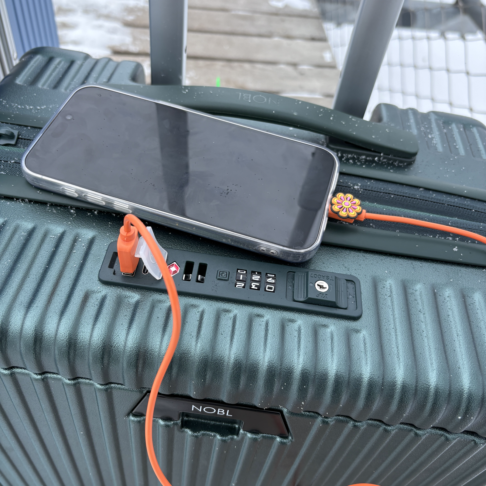 Traveler charging a phone from a silver NOBL carry-on