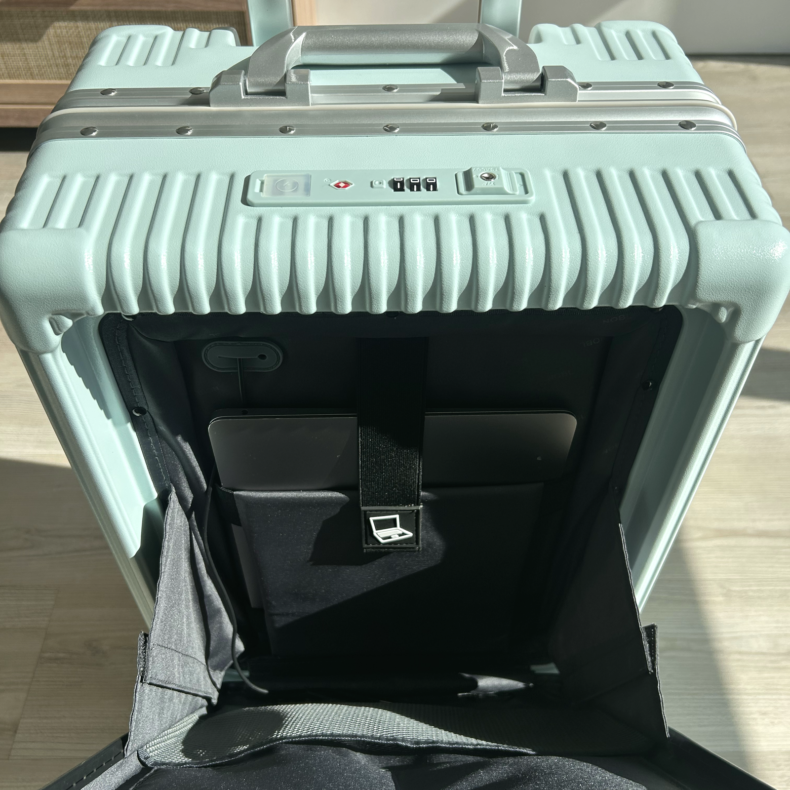 Open front laptop pocket on a green NOBL carry-on for fast airport access
