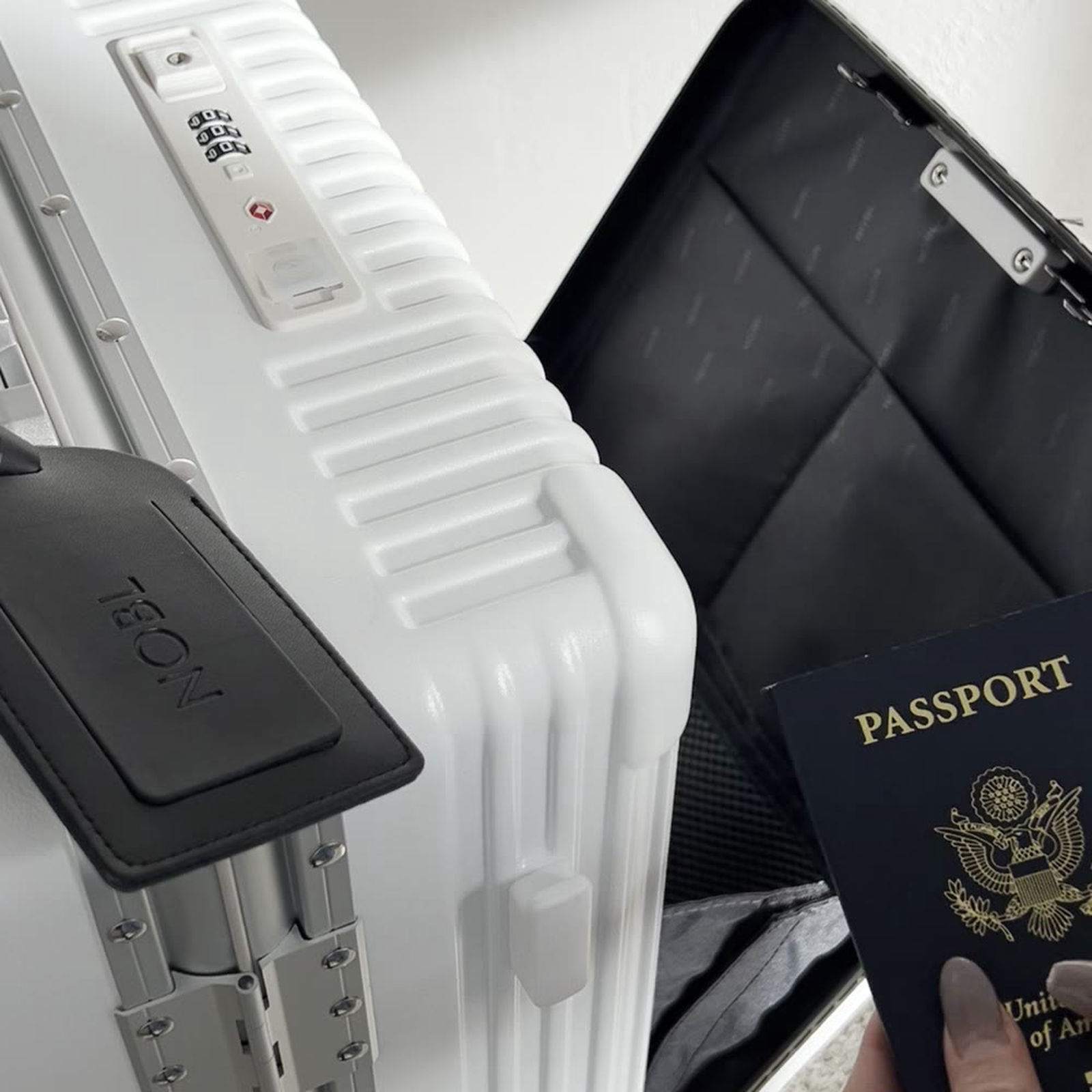 White NOBL carry-on beside a passport and luggage tag for fast document access
